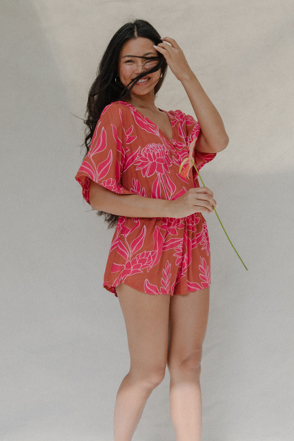 woman with brown hair wearing a sienna colored playsuit with mid length sleeves and awapuhi pattern