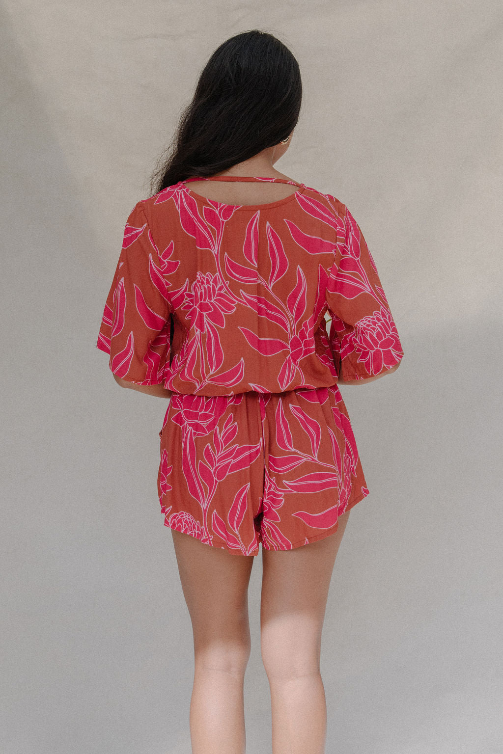 woman with brown hair wearing a sienna colored playsuit with mid length sleeves and awapuhi pattern