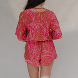 woman with brown hair wearing a sienna colored playsuit with mid length sleeves and awapuhi pattern