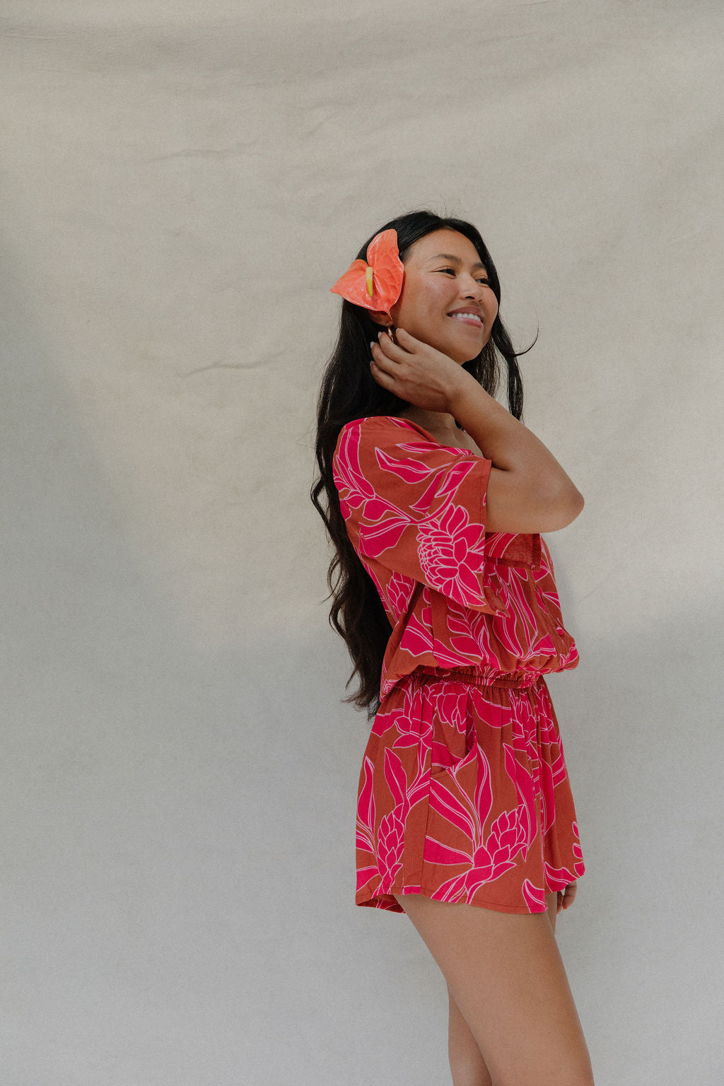 woman with brown hair wearing a sienna colored playsuit with mid length sleeves and awapuhi pattern