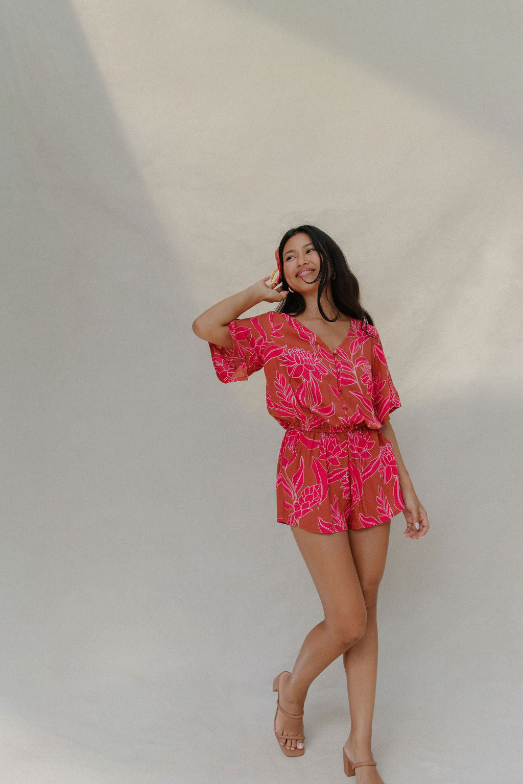 woman with brown hair wearing a sienna colored playsuit with mid length sleeves and awapuhi pattern