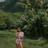 woman with brown hair wearing a navy playsuit with bright pink hibiscus print