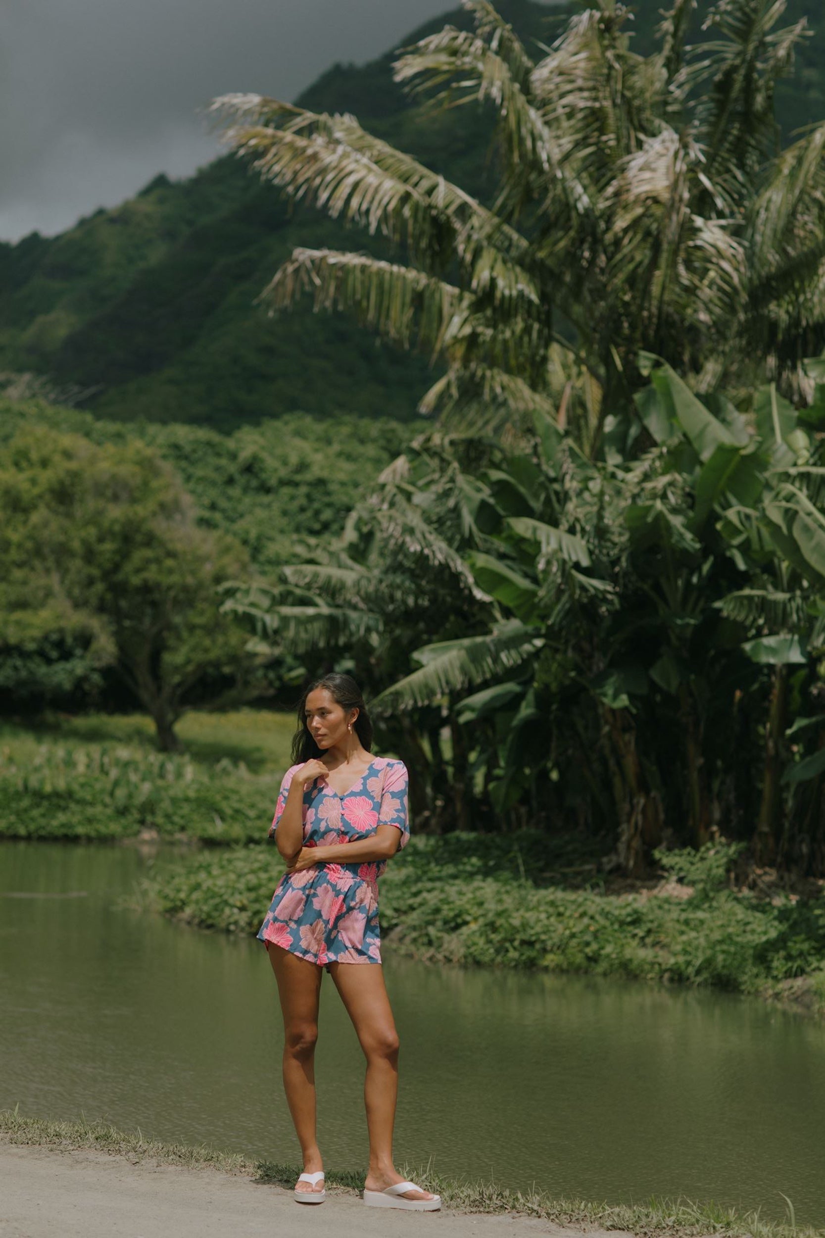 woman with brown hair wearing a navy playsuit with bright pink hibiscus print