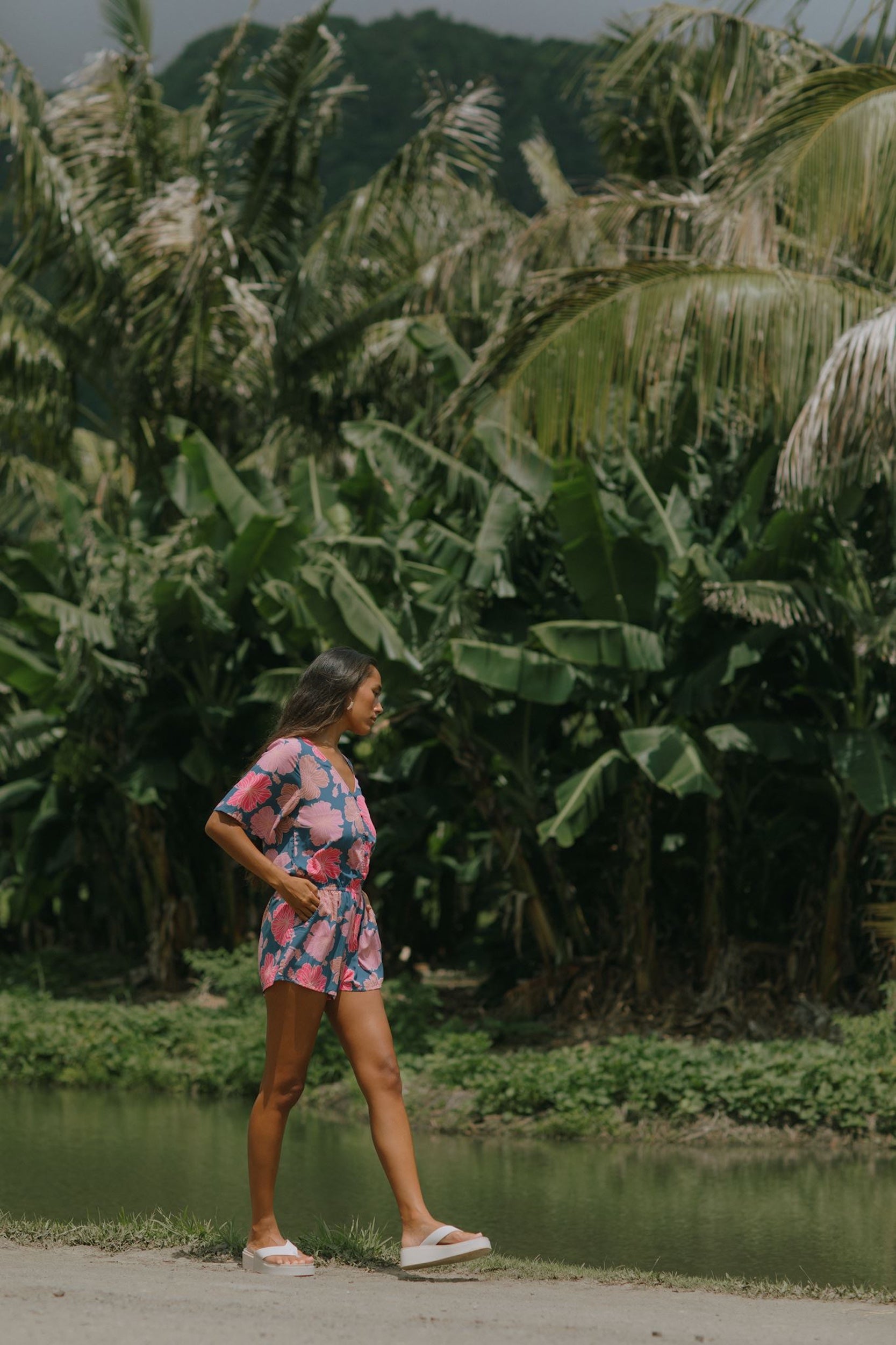 woman with brown hair wearing a navy playsuit with bright pink hibiscus print