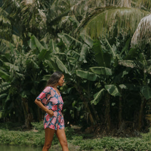 woman with brown hair wearing a navy playsuit with bright pink hibiscus print