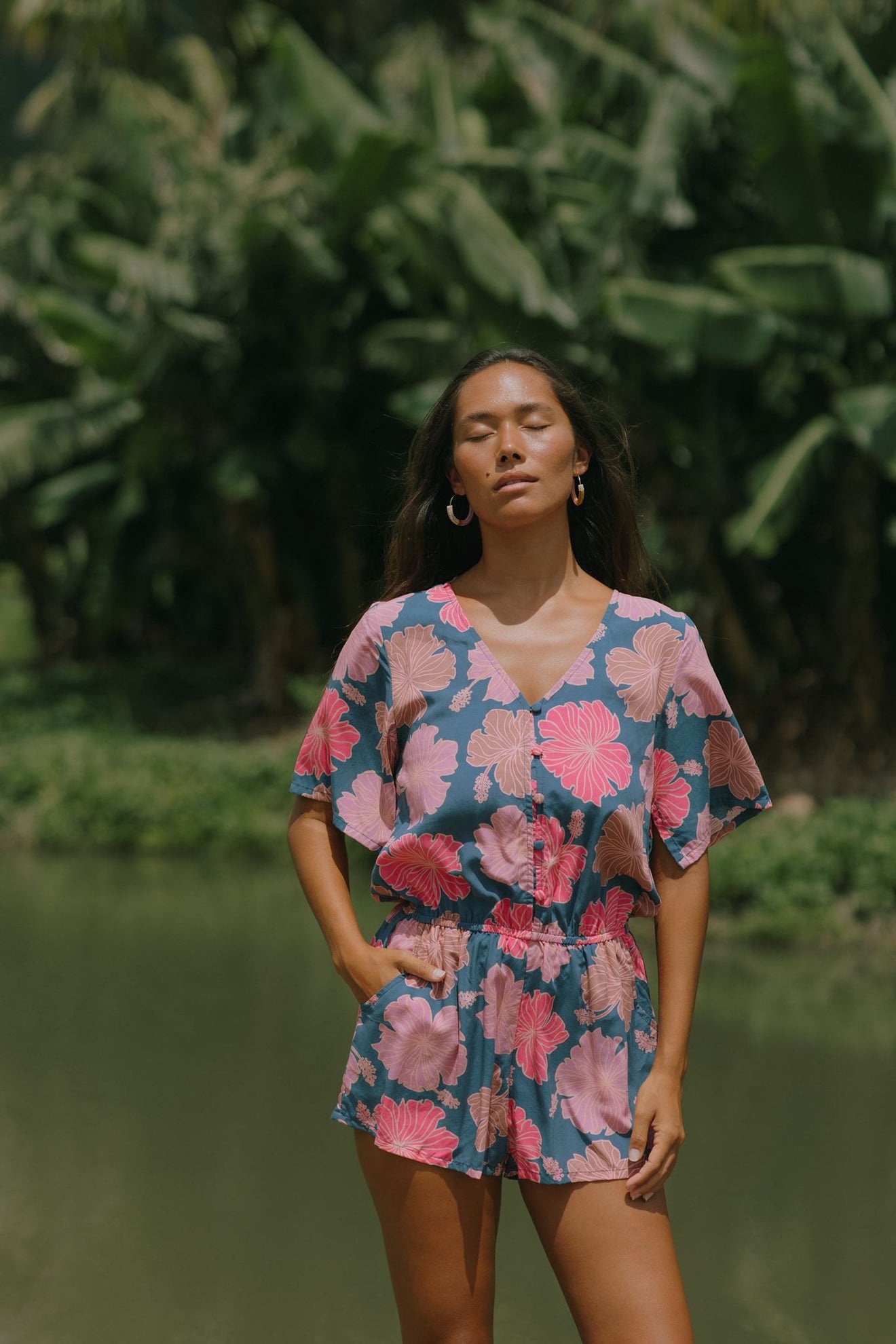 woman with brown hair wearing a navy playsuit with bright pink hibiscus print