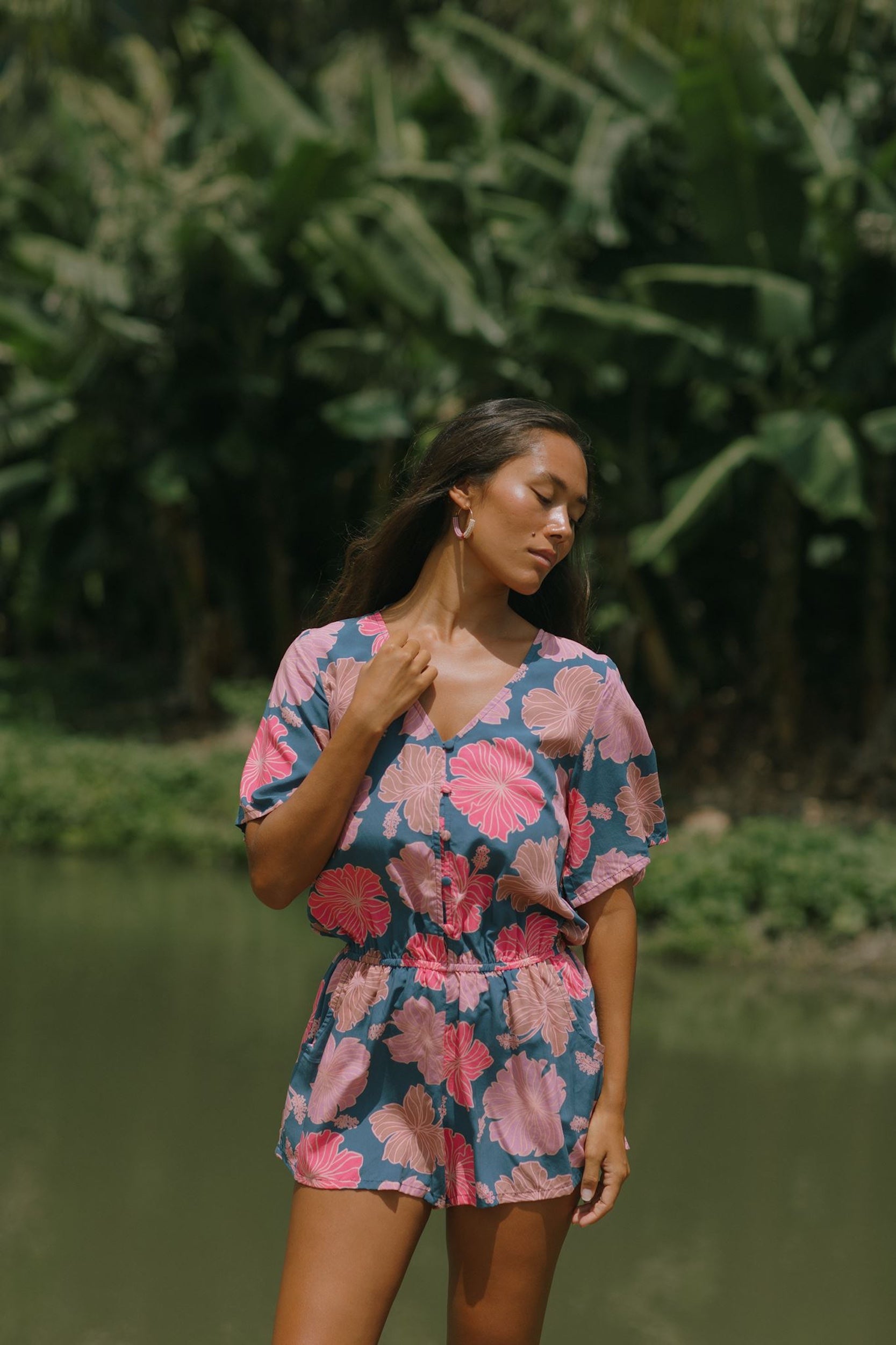 woman with brown hair wearing a navy playsuit with bright pink hibiscus print