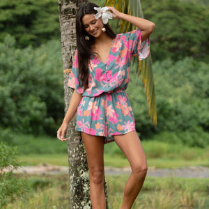 woman with brown hair wearing a teal playsuit with orange and pink floral print