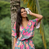 woman with brown hair wearing a teal playsuit with orange and pink floral print
