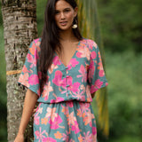 woman with brown hair wearing a teal playsuit with orange and pink floral print