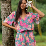 woman with brown hair wearing a teal playsuit with orange and pink floral print