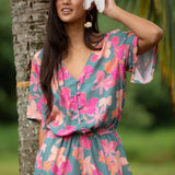 woman with brown hair wearing a teal playsuit with orange and pink floral print