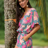 woman with brown hair wearing a teal playsuit with orange and pink floral print