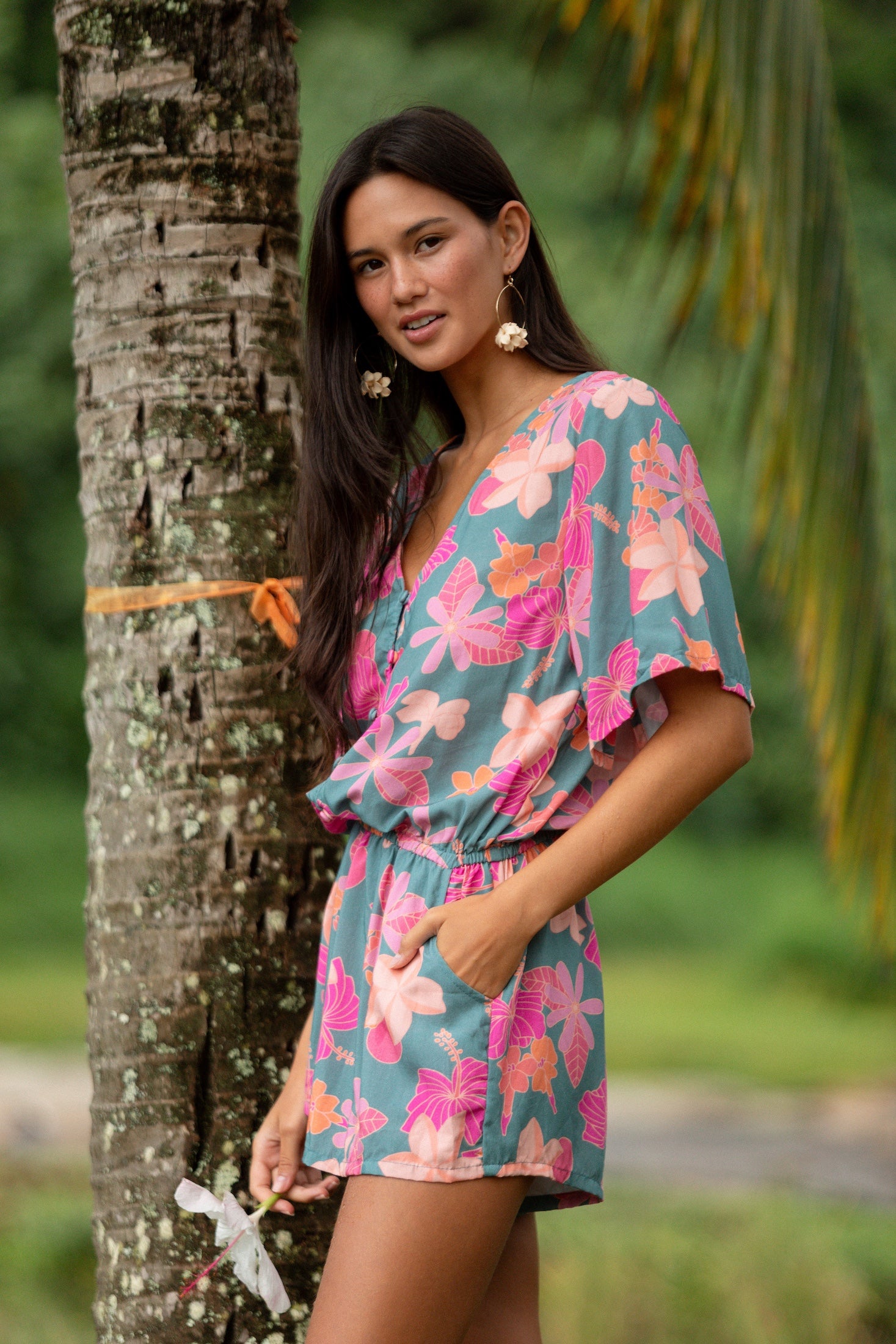 woman with brown hair wearing a teal playsuit with orange and pink floral print