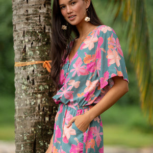 woman with brown hair wearing a teal playsuit with orange and pink floral print