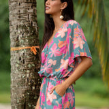 woman with brown hair wearing a teal playsuit with orange and pink floral print