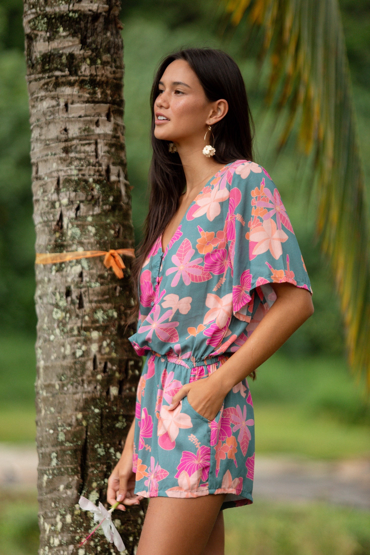 woman with brown hair wearing a teal playsuit with orange and pink floral print