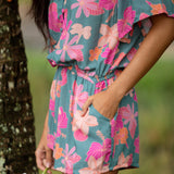 woman with brown hair wearing a teal playsuit with orange and pink floral print