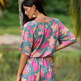 woman with brown hair wearing a teal playsuit with orange and pink floral print