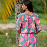 woman with brown hair wearing a teal playsuit with orange and pink floral print