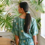 woman with brown hair wearing lush green playsuit with puakenikeni
