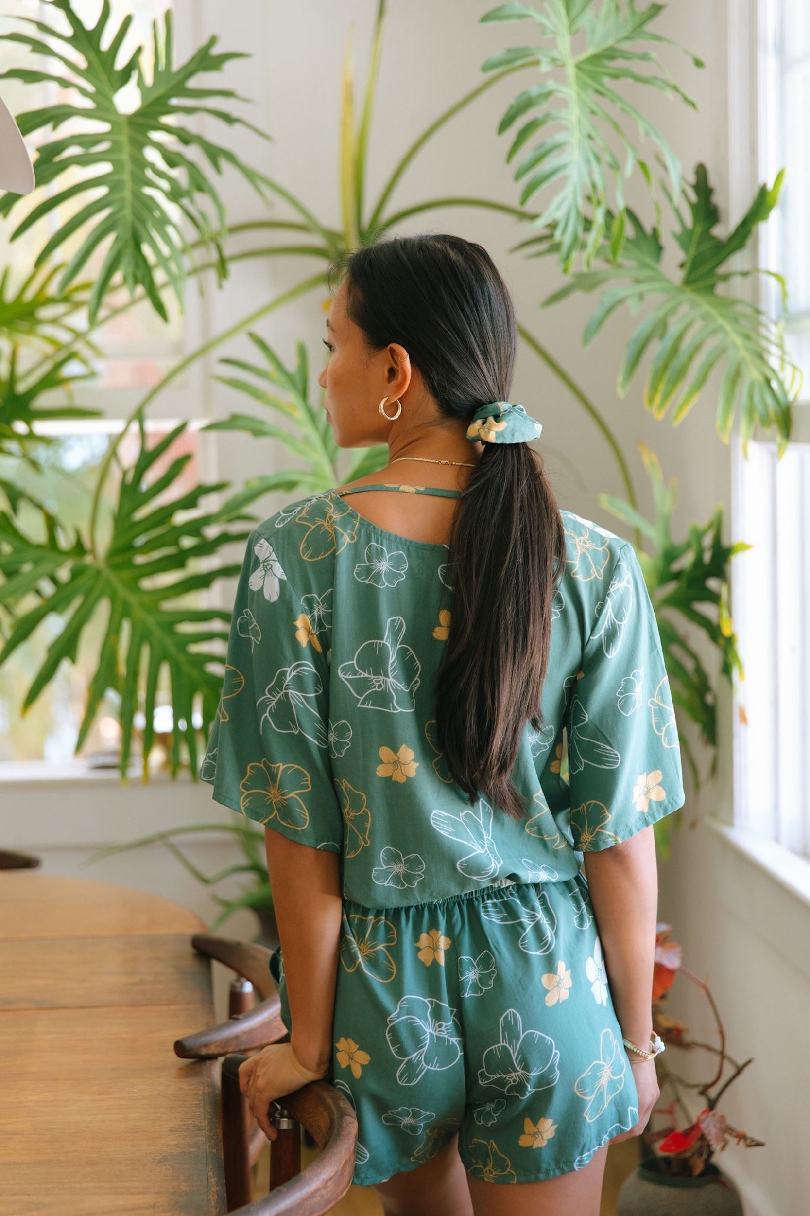 woman with brown hair wearing lush green playsuit with puakenikeni