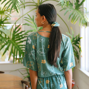 woman with brown hair wearing lush green playsuit with puakenikeni