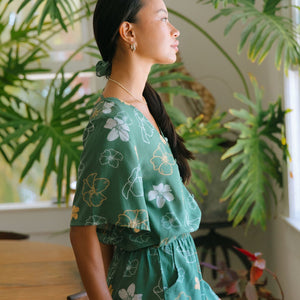 woman with brown hair wearing lush green playsuit with puakenikeni