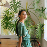 woman with brown hair wearing lush green playsuit with puakenikeni