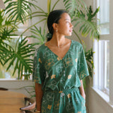 woman with brown hair wearing lush green playsuit with puakenikeni