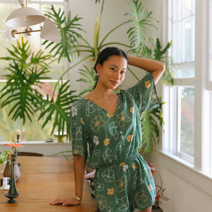 woman with brown hair wearing lush green playsuit with puakenikeni