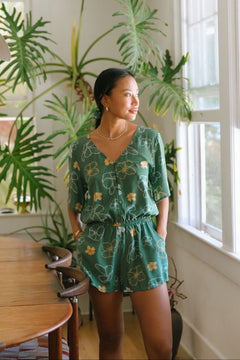 woman with brown hair wearing lush green playsuit with puakenikeni