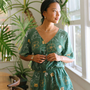 woman with brown hair wearing lush green playsuit with puakenikeni