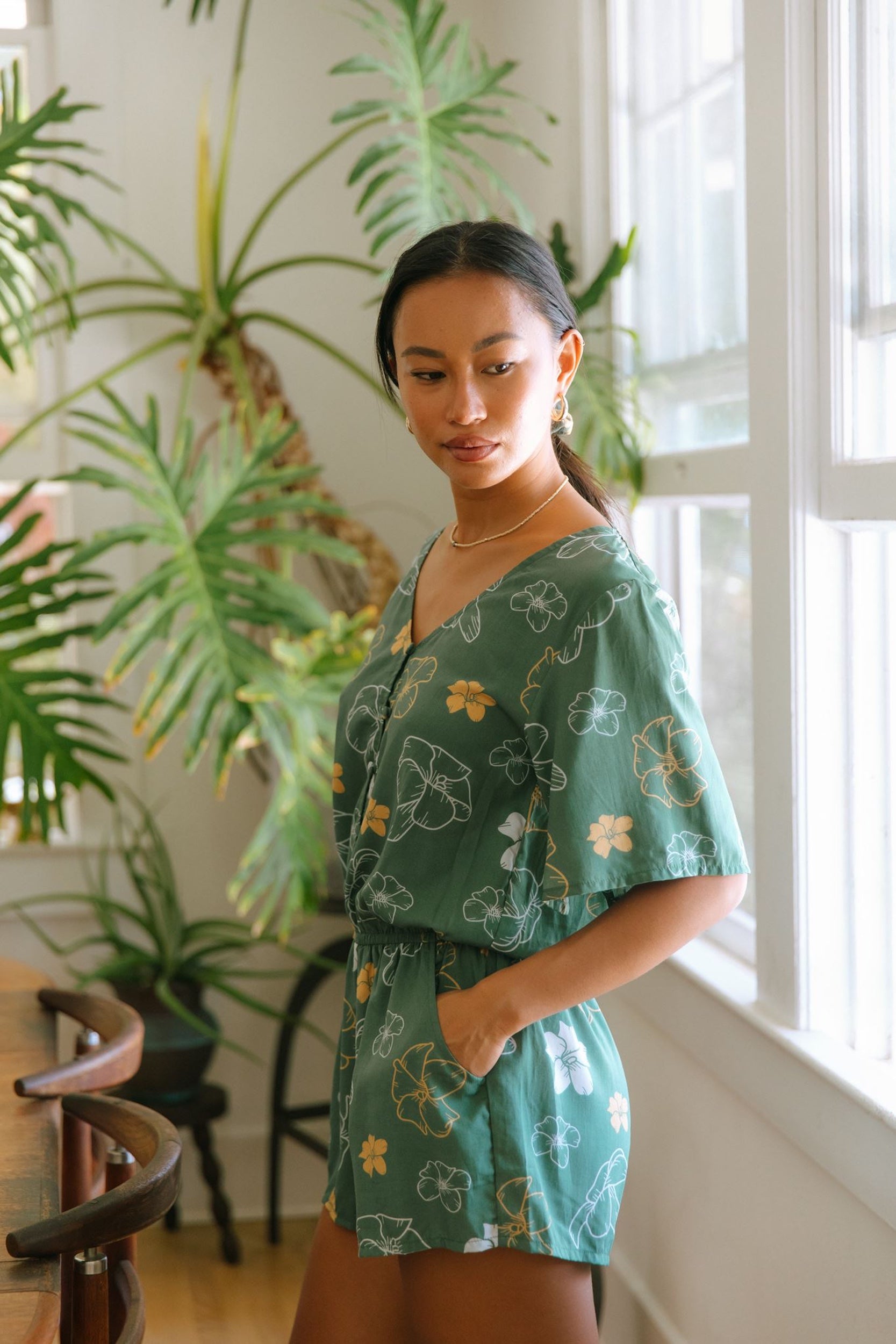 woman with brown hair wearing lush green playsuit with puakenikeni