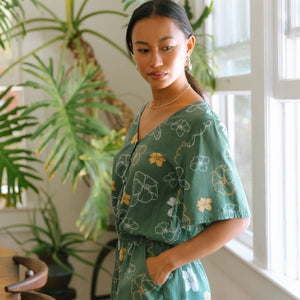 woman with brown hair wearing lush green playsuit with puakenikeni