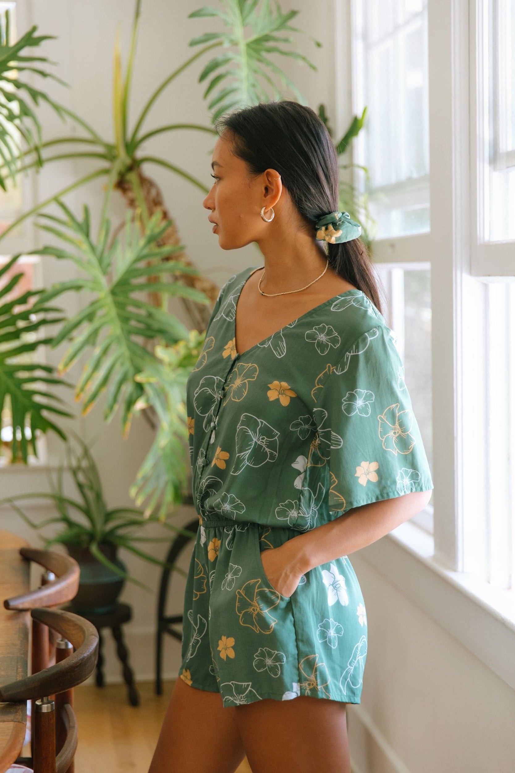 woman with brown hair wearing lush green playsuit with puakenikeni