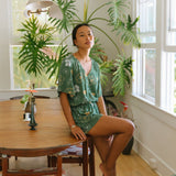 woman with brown hair wearing lush green playsuit with puakenikeni