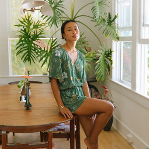 woman with brown hair wearing lush green playsuit with puakenikeni