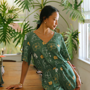 woman with brown hair wearing lush green playsuit with puakenikeni