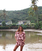 Woman with brown hair wearing a flowy button up playsuit in blush and brown hibiscus print.