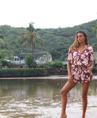 Woman with brown hair wearing a flowy button up playsuit in blush and brown hibiscus print.