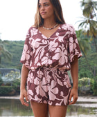 Woman with brown hair wearing a flowy button up playsuit in blush and brown hibiscus print.