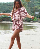 Woman with brown hair wearing a flowy button up playsuit in blush and brown hibiscus print.