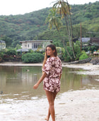 Woman with brown hair wearing a flowy button up playsuit in blush and brown hibiscus print.