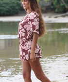 Woman with brown hair wearing a flowy button up playsuit in blush and brown hibiscus print.