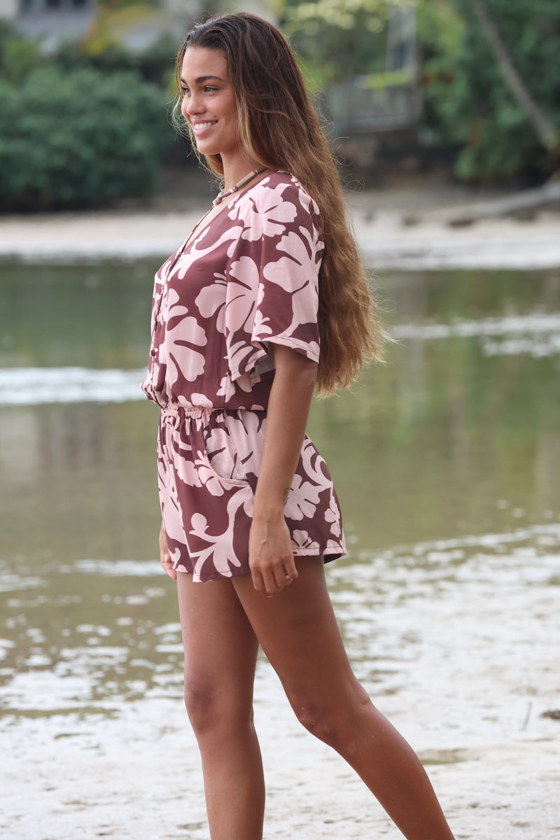 Woman with brown hair wearing a flowy button up playsuit in blush and brown hibiscus print.
