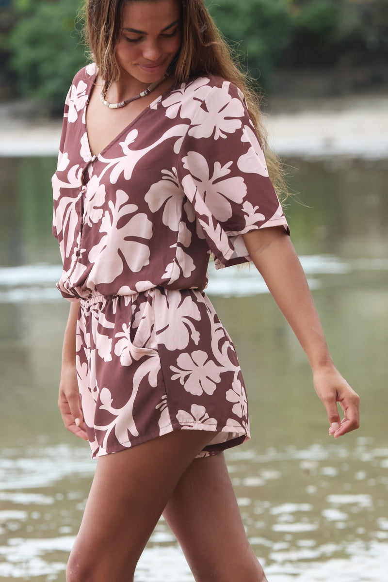 Woman with brown hair wearing a flowy button up playsuit in blush and brown hibiscus print.