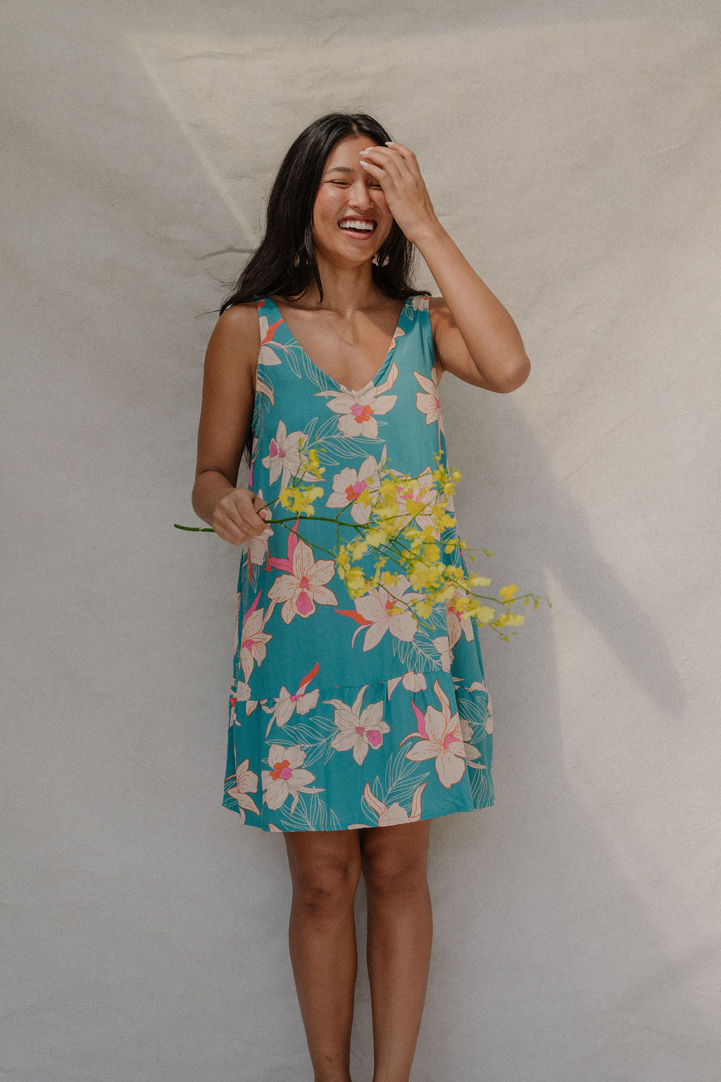 woman with brown hair wearing a teal v neck dress with ruffle hem and orchid pattern