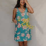 woman with brown hair wearing a teal v neck dress with ruffle hem and orchid pattern