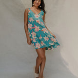 woman with brown hair wearing a teal v neck dress with ruffle hem and orchid pattern